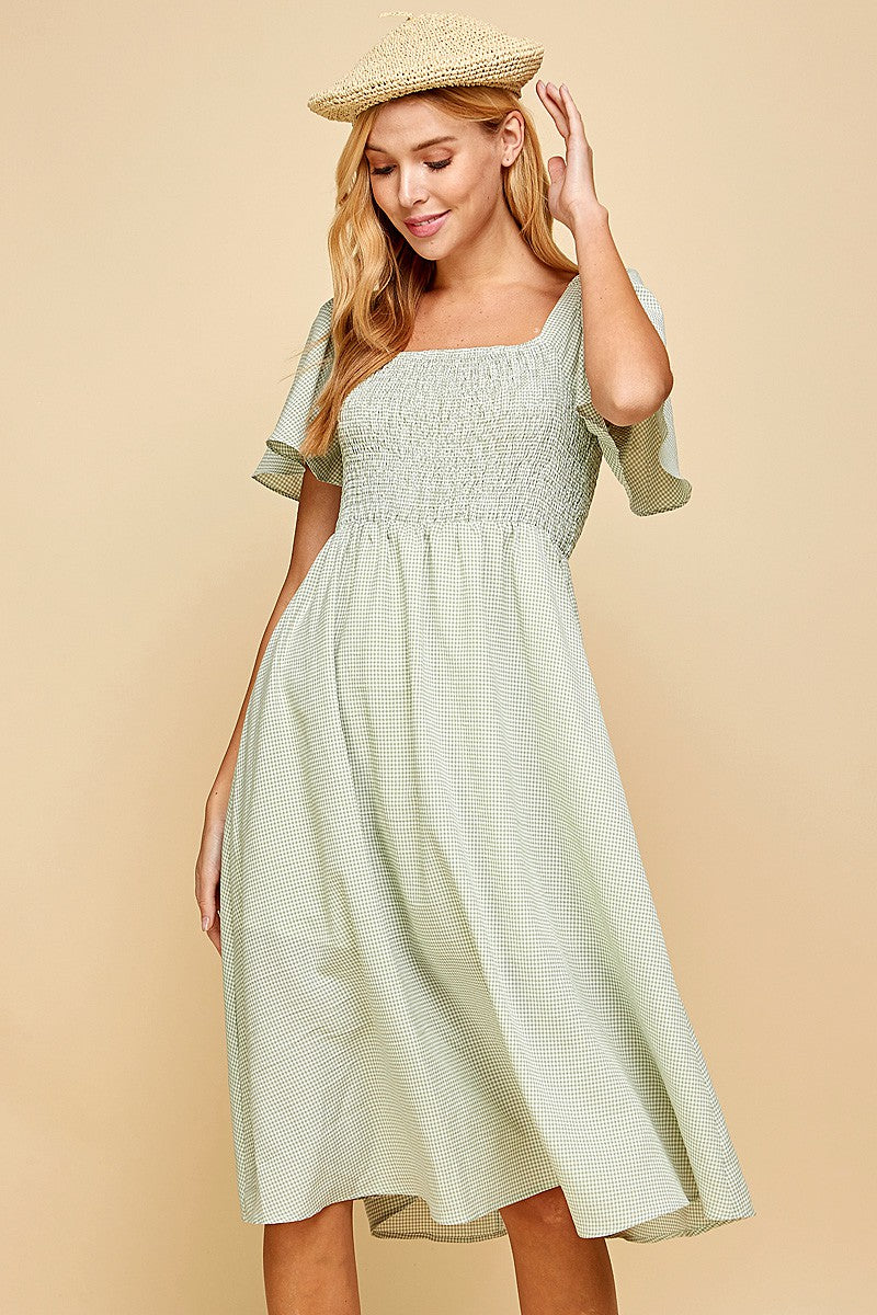 woman wearing a green gingham dress with a square neckline and flutter sleeves, styled with a straw hat