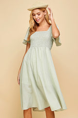 woman wearing a green gingham dress with a square neckline and flutter sleeves, styled with a straw hat