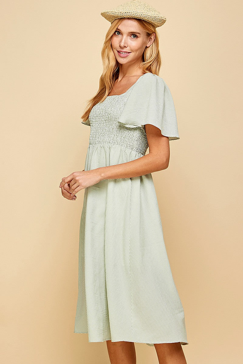 woman wearing a light green gingham midi dress with short smocked sleeves and a square neckline, styled with a straw hat