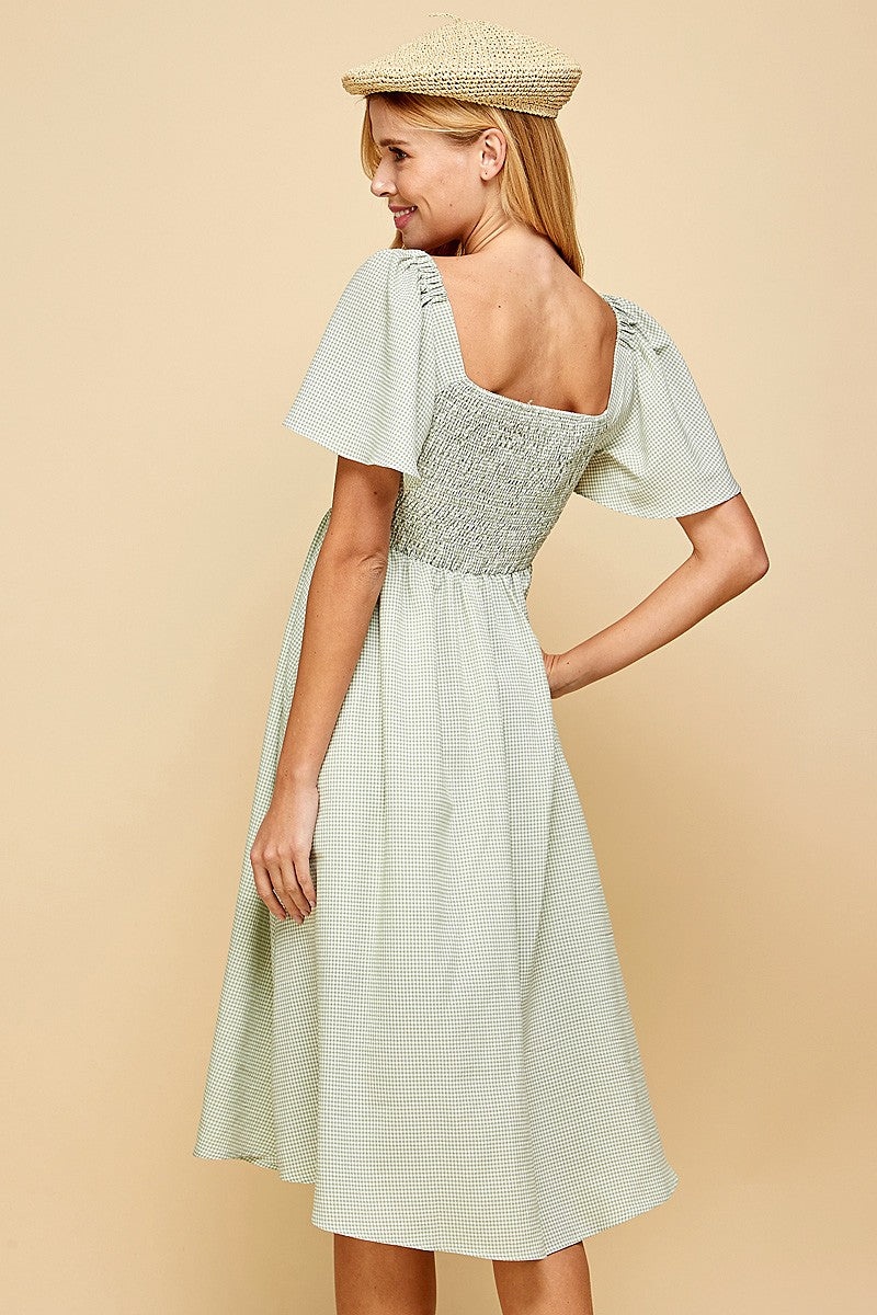 woman wearing a green gingham smocked back dress with short flutter sleeves and a midi length