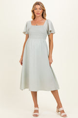 woman wearing a light green maternity dress with a square neckline and short flutter sleeves