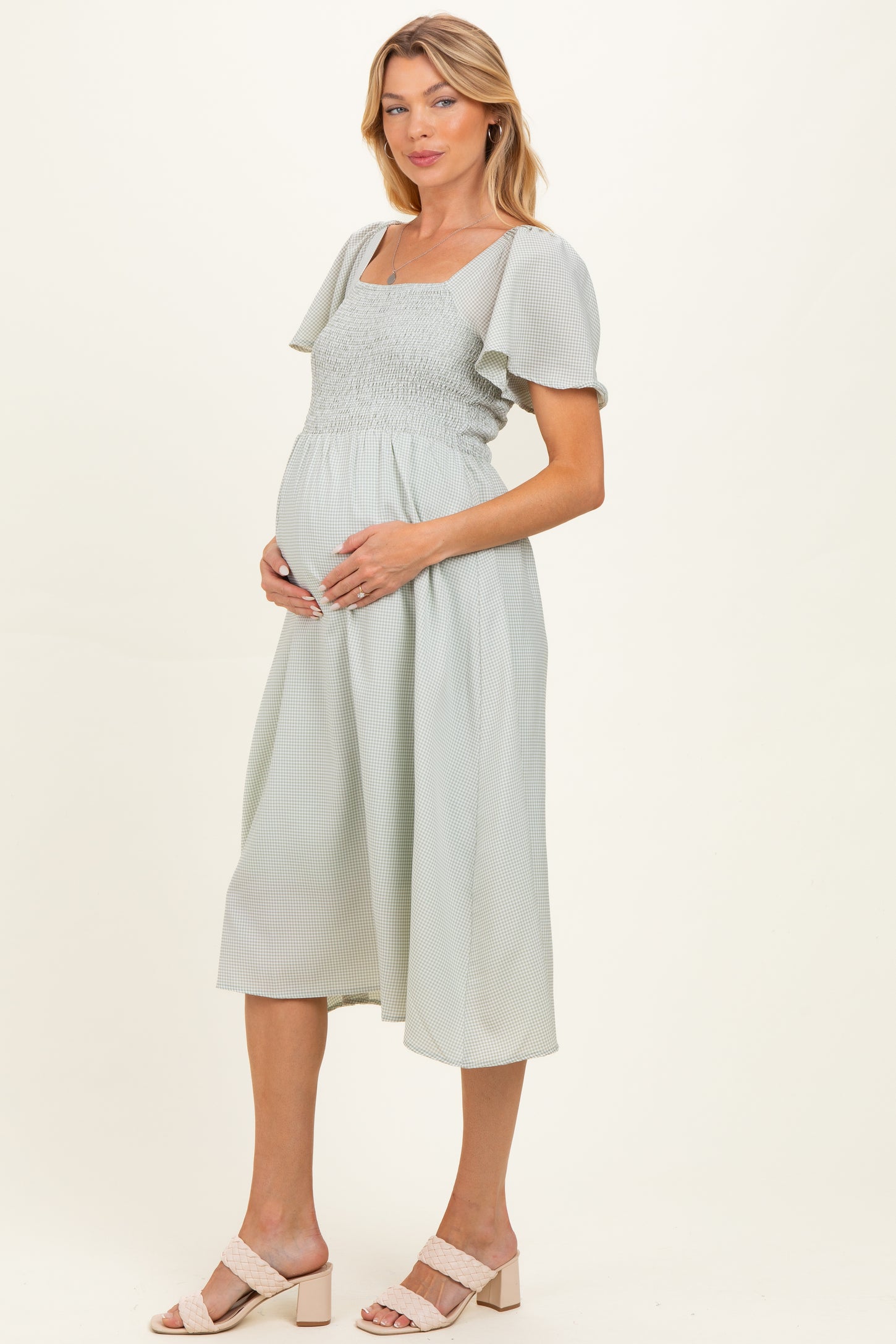 woman wearing a light green maternity dress with short puff sleeves and smocked bodice, holding her baby bump