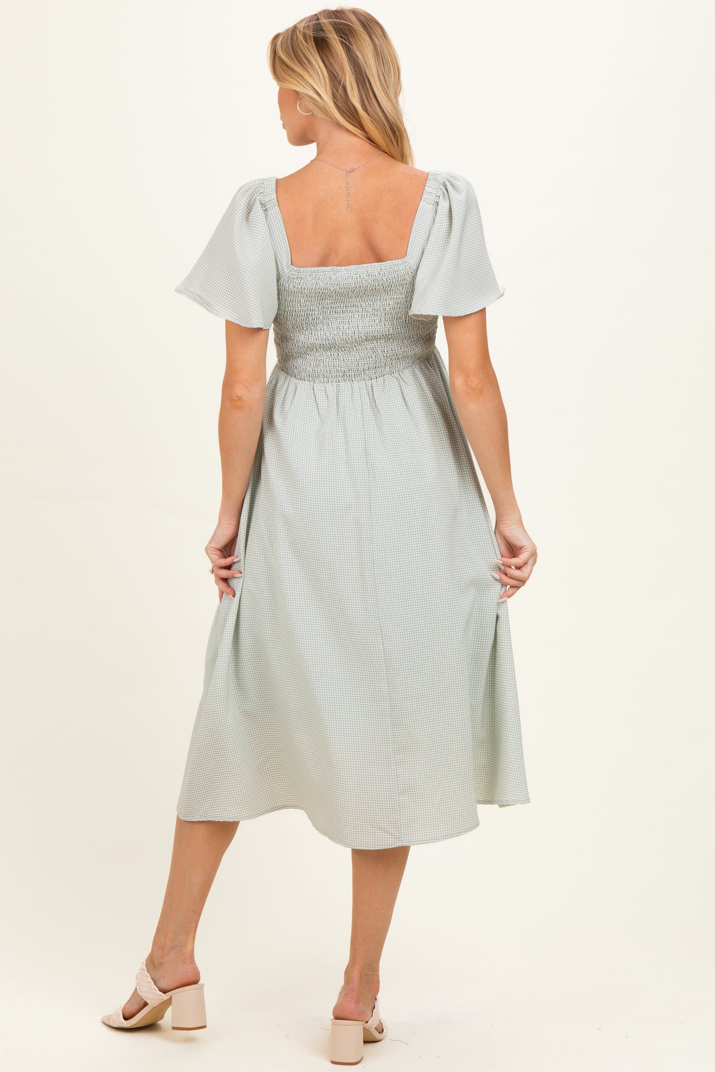 woman wearing a light gray maternity dress with short flutter sleeves and a smocked back, showing her baby bump