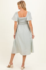 woman wearing a light gray maternity dress with short flutter sleeves and a smocked back, showing her baby bump