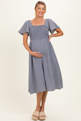 woman wearing a navy and white striped maternity dress with short flutter sleeves and a smocked bodice, holding her baby bump