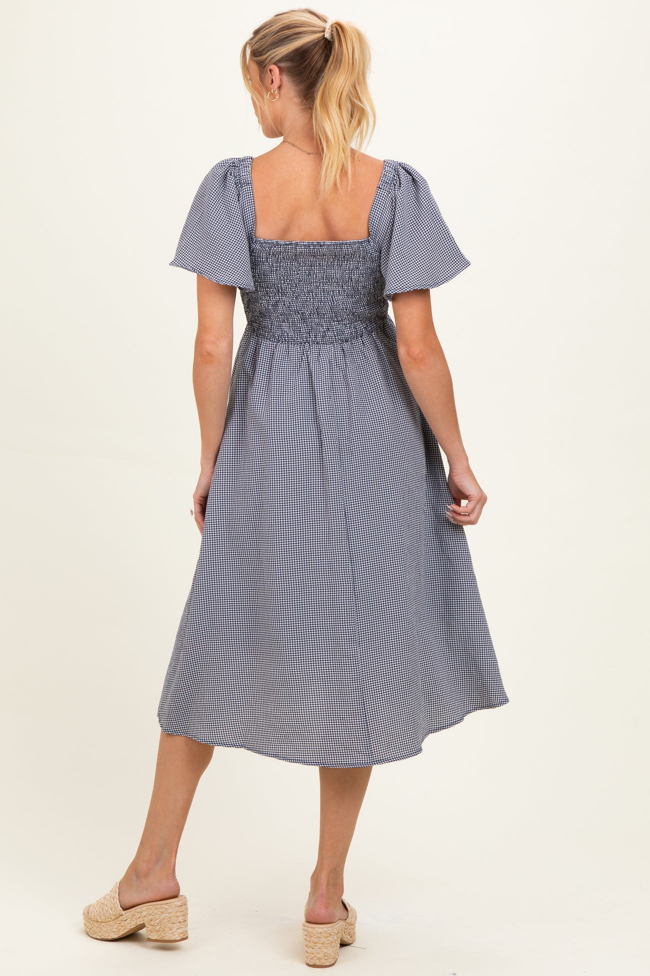 woman wearing a striped maternity dress with smocked bodice and flutter sleeves, showing a relaxed fit and mid-length hem
