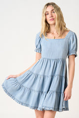 woman wearing a light blue tiered denim dress with short puff sleeves and a square neckline