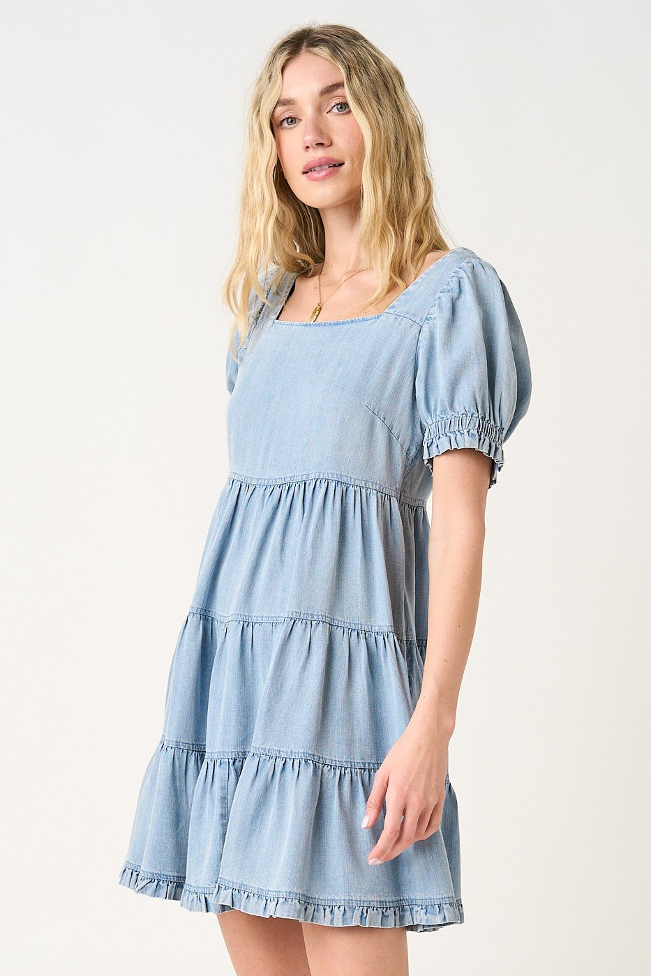 woman wearing a light blue short puff sleeve tiered denim dress with a square neckline