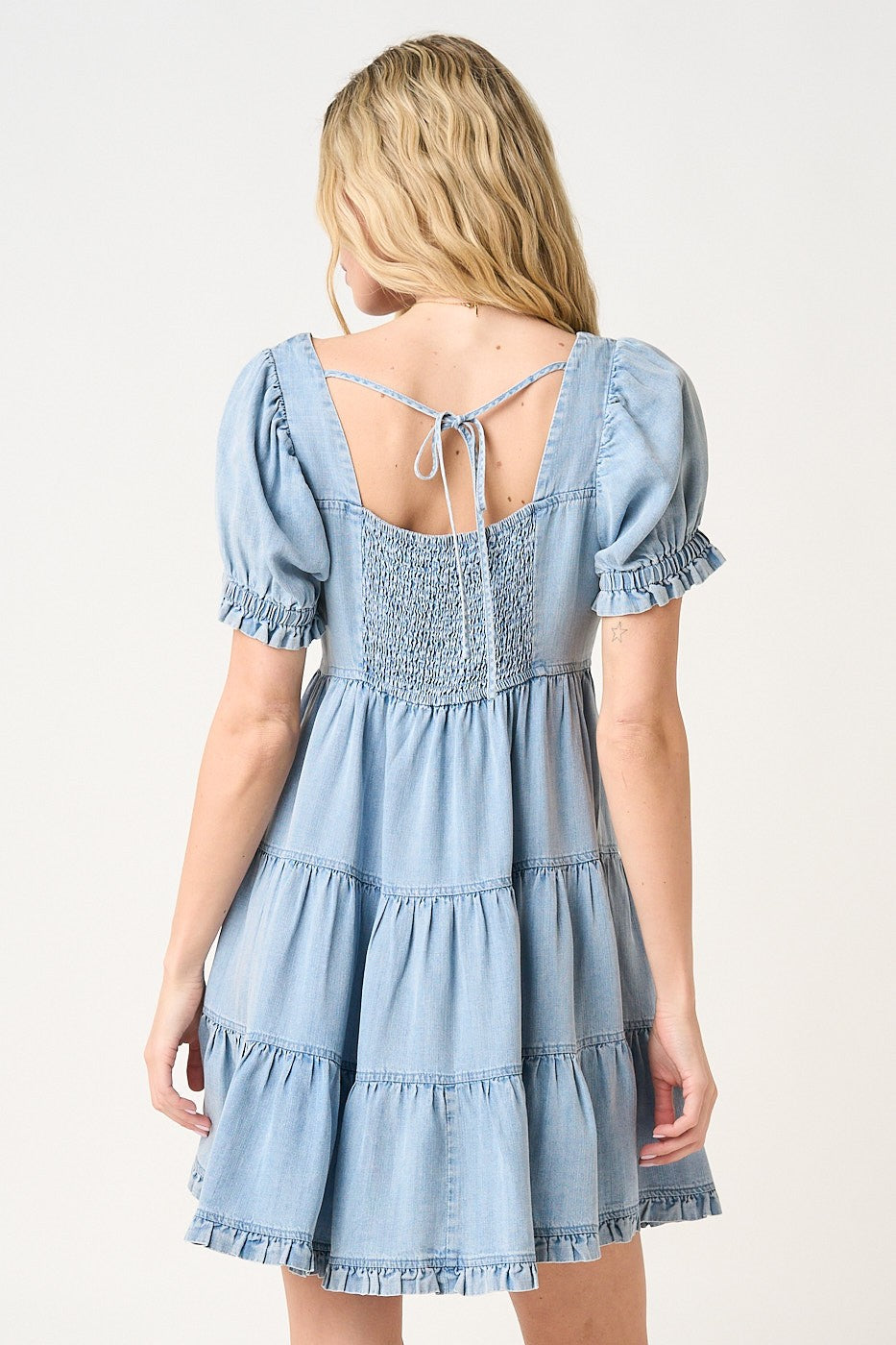 woman wearing a light blue tiered denim dress with short puff sleeves and a tie-back detail