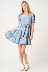 woman wearing a light blue chambray tiered dress with puff sleeves and a square neckline