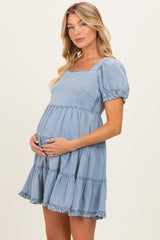 woman wearing a light blue short sleeve maternity dress with a square neckline and ruffled hem, holding her baby bump