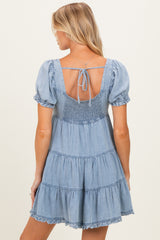 woman wearing a light blue maternity dress with short puff sleeves and a tiered skirt, showing a smocked back detail