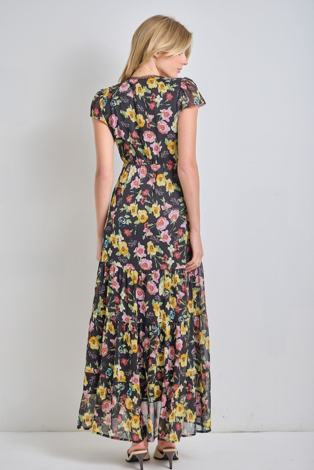 woman wearing a floral maxi dress with short sleeves and a tiered skirt, shown from the back.