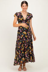 woman wearing a black floral maternity maxi dress and holding her baby bump