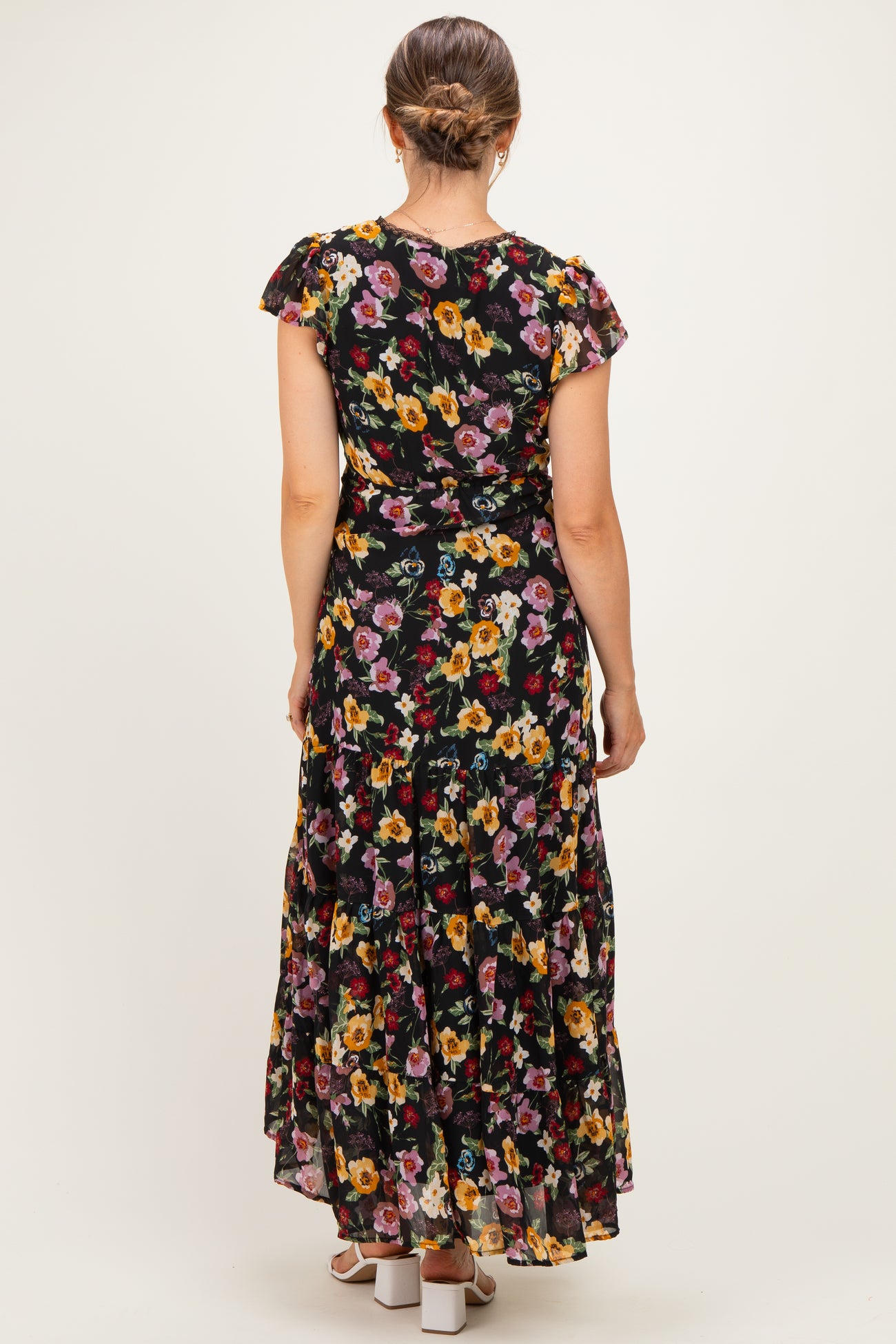 woman wearing a black floral maternity maxi dress with ruffle sleeves, showing the back view