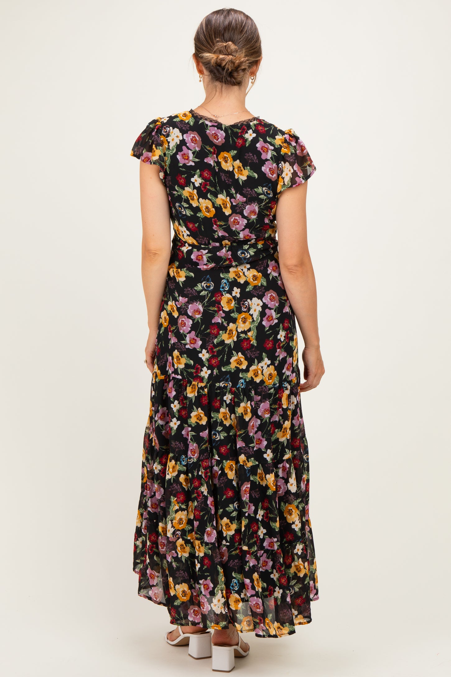 woman wearing a black floral maternity maxi dress with ruffle sleeves, showing the back view