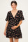woman wearing a black floral maternity dress with a deep v-neck and puff sleeves, holding her baby bump