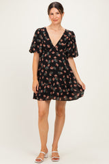 woman wearing a black floral maternity dress with a deep v-neck and puff sleeves, holding the hem with one hand
