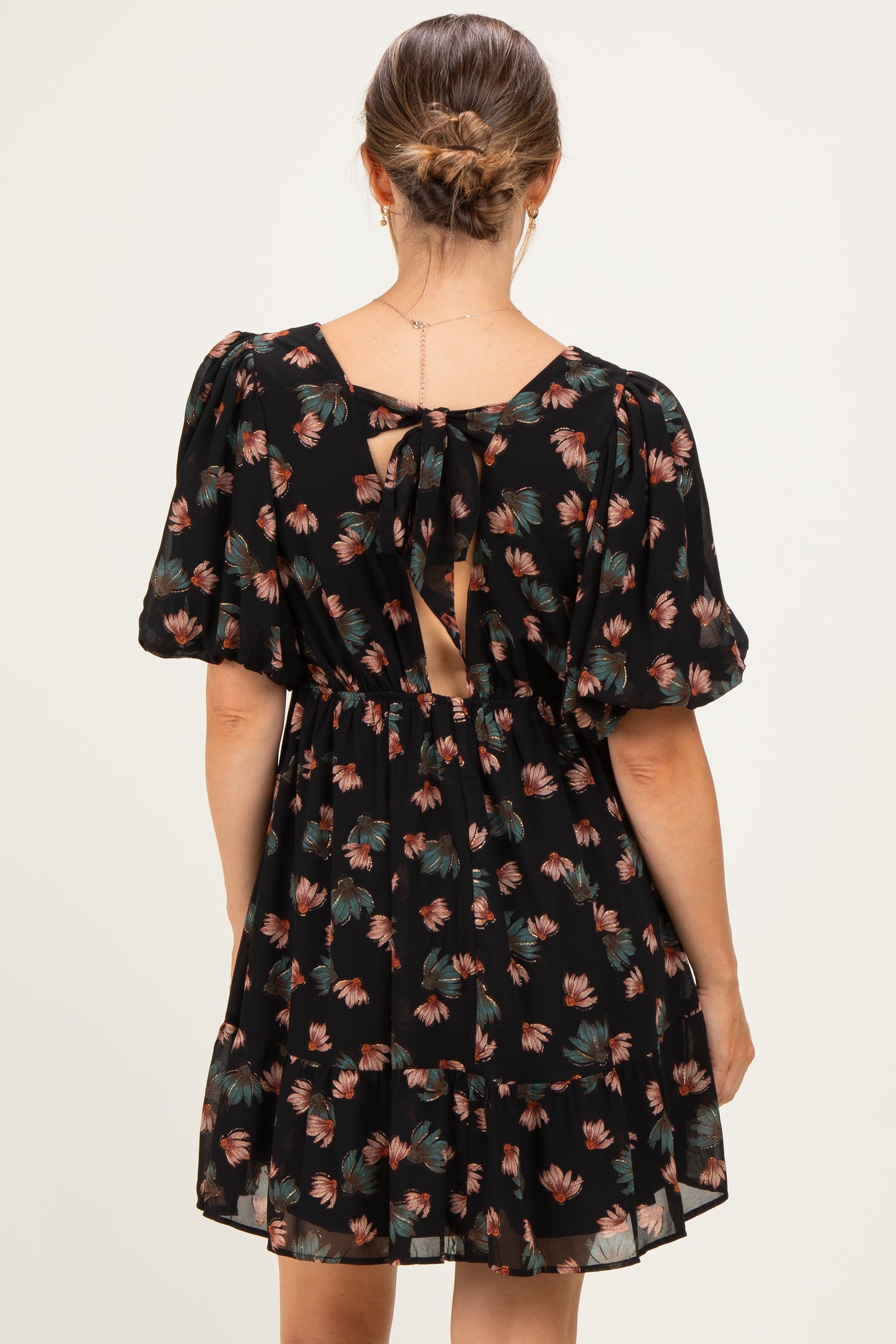 woman wearing a black floral maternity dress with puff sleeves and an open back detail
