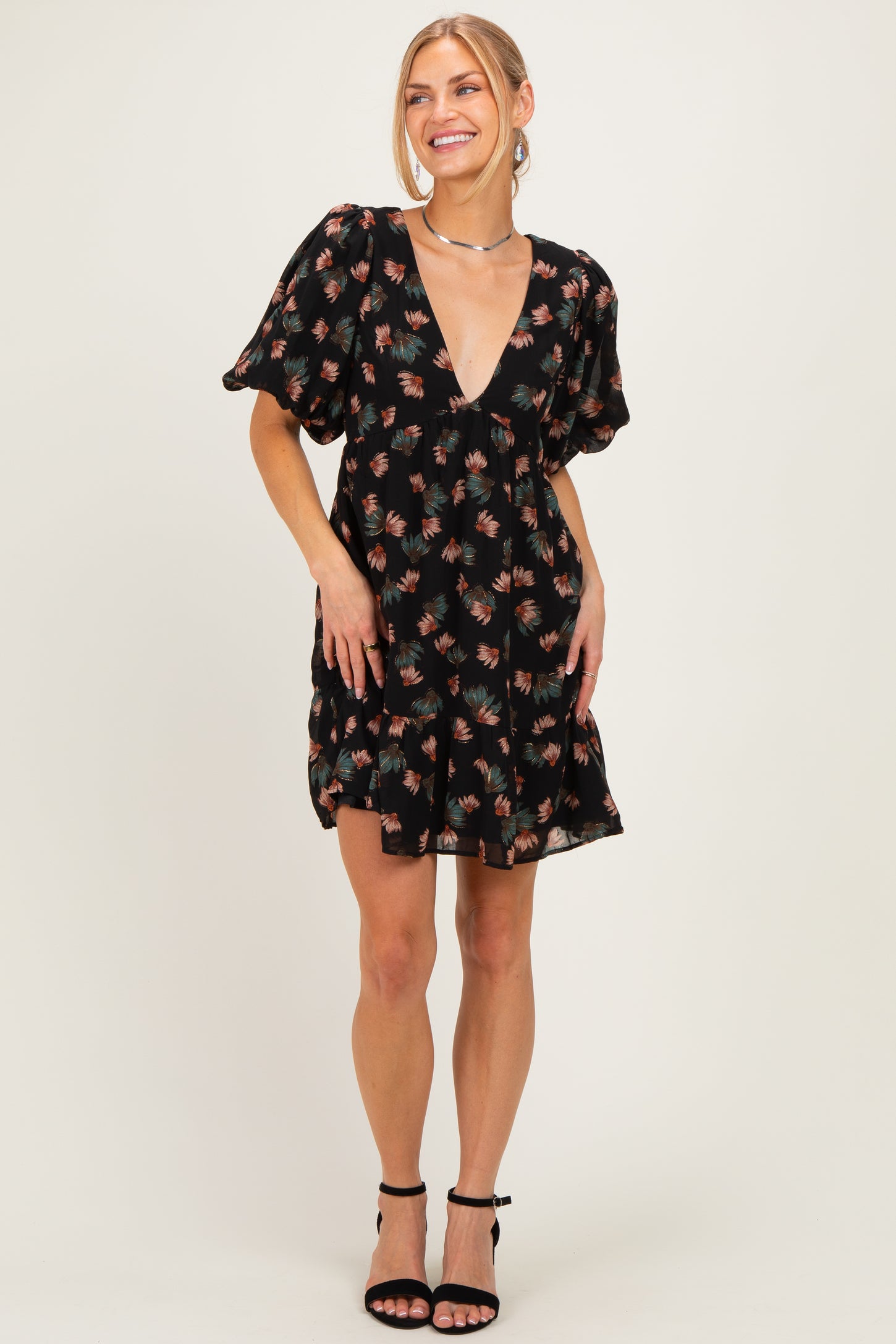 woman wearing a black floral mini dress with a deep v-neck and puff sleeves, standing and smiling