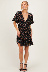 woman wearing a black floral mini dress with a deep v-neck and puff sleeves, standing and smiling