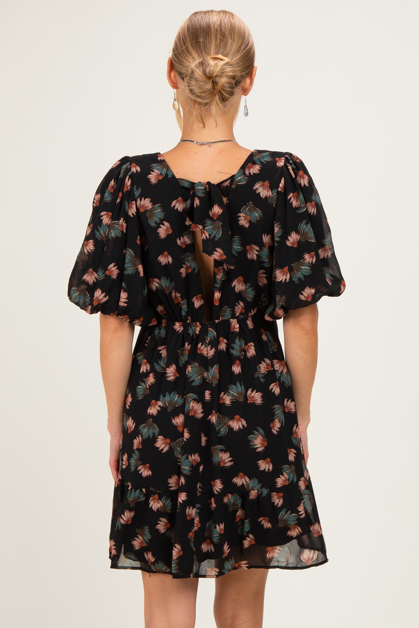 woman wearing a black floral print dress with puff sleeves and a tie-back detail, shown from the back