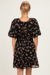 woman wearing a black floral print dress with puff sleeves and a tie-back detail, shown from the back