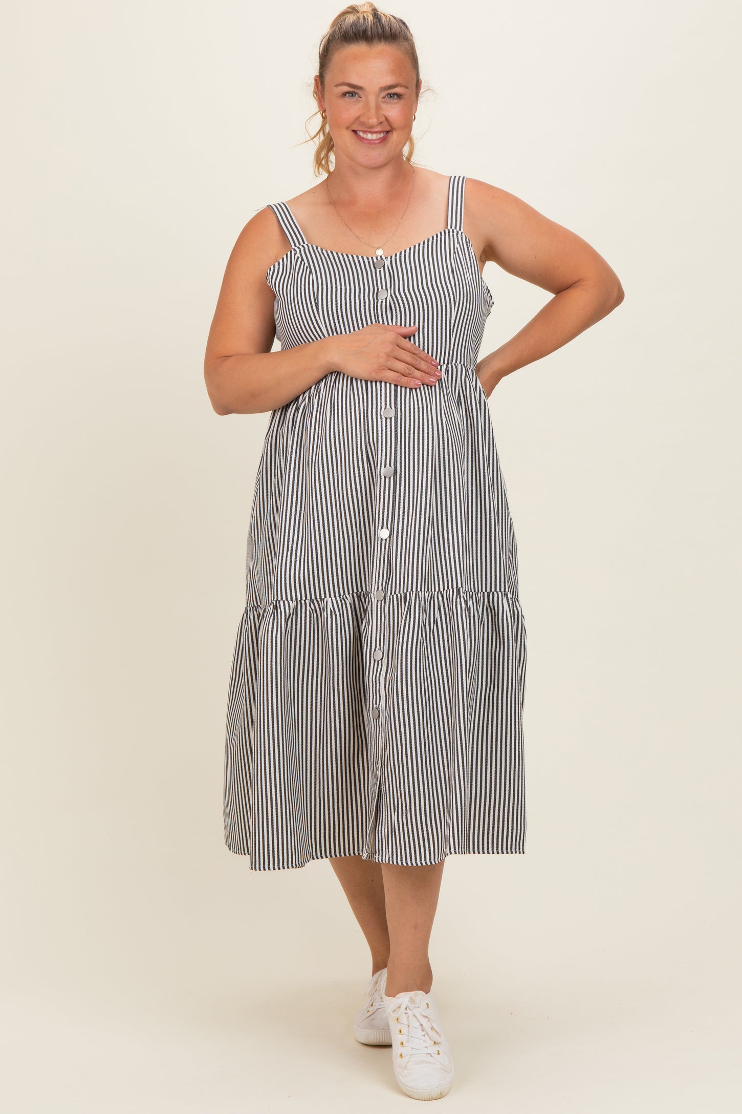 woman wearing a striped maternity plus dress with a button front and tiered skirt, holding her baby bump