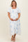 woman wearing a white maternity plus dress with blue floral patterns and holding her baby bump
