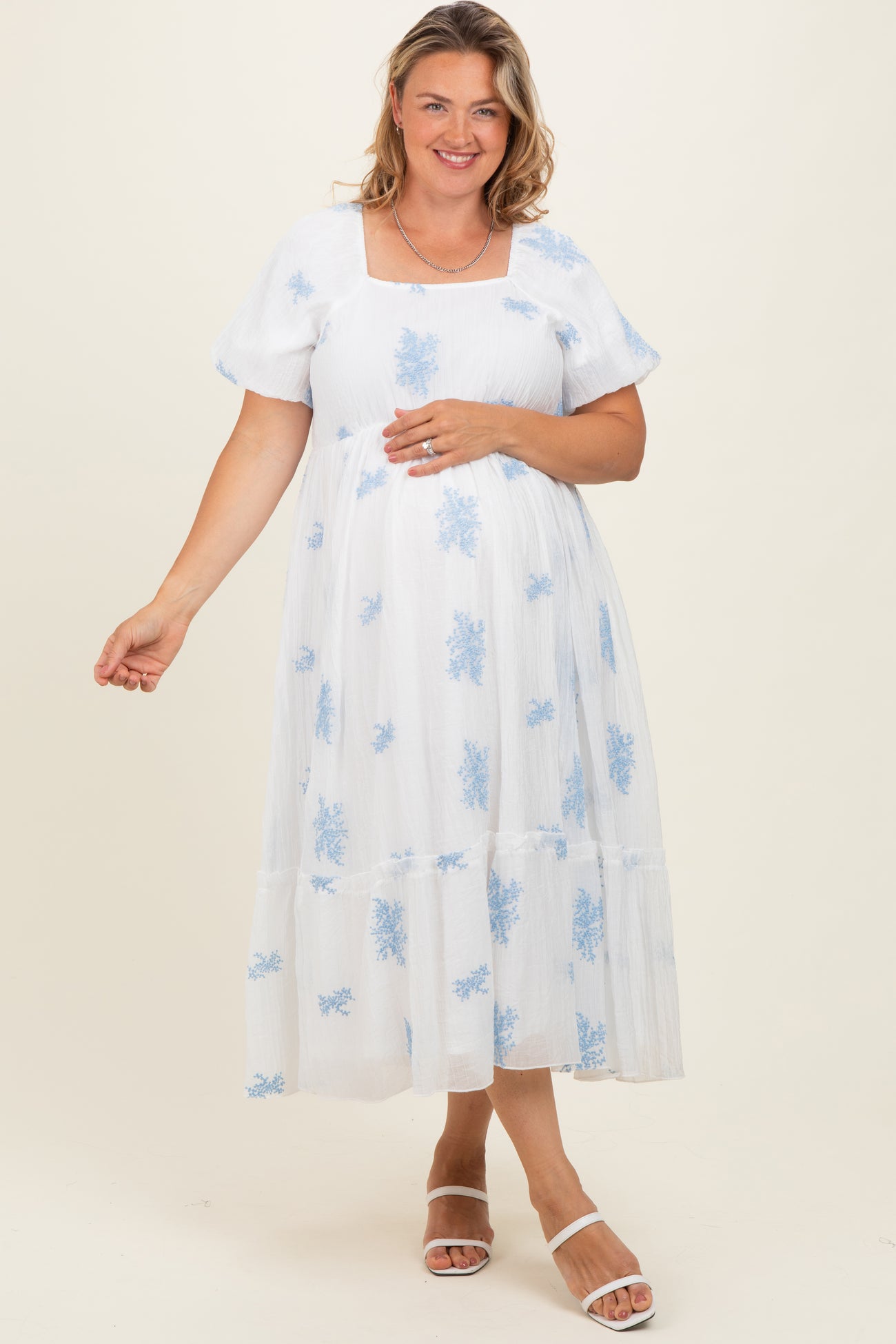 woman wearing a white and blue floral maternity dress with short sleeves and a tiered hem, showing her baby bump