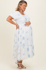 woman wearing a white maternity plus dress with blue floral embroidery and holding her baby bump