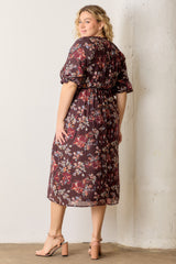woman wearing a burgundy floral plus-size midi dress with puff sleeves and a cinched waist, standing sideways against a wall