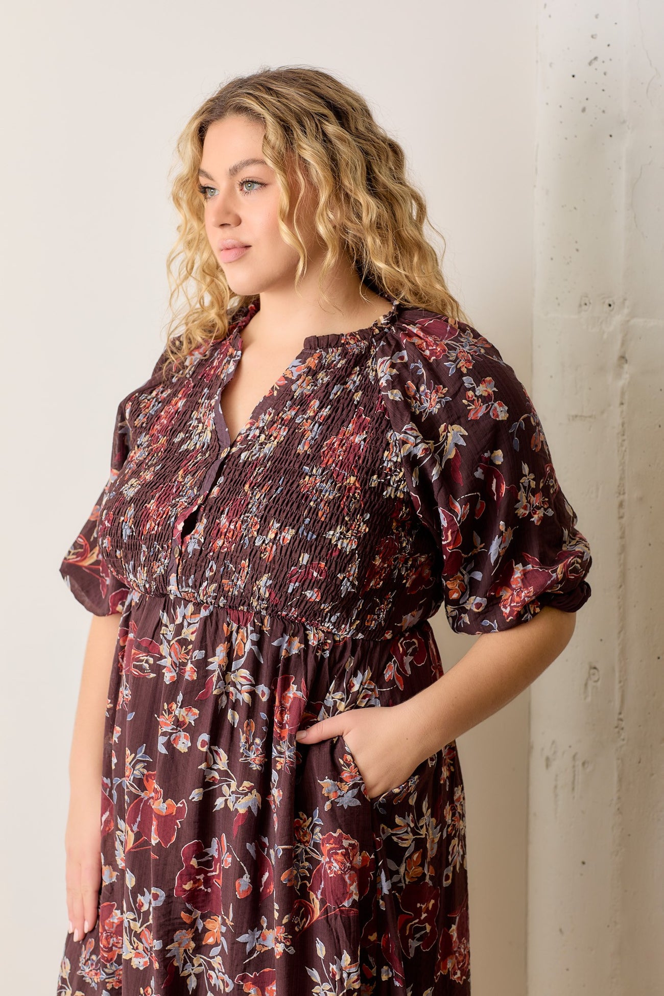 plus size woman wearing a burgundy floral smocked dress with short puff sleeves and side pockets