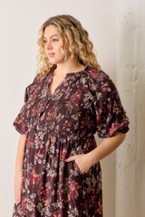 plus size woman wearing a burgundy floral smocked dress with short puff sleeves and side pockets