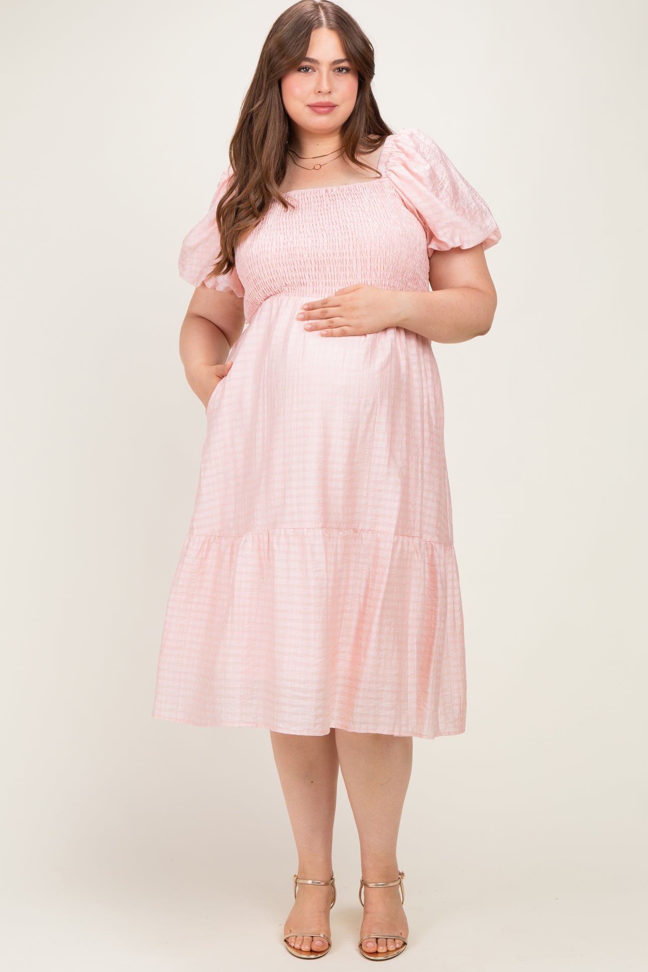 woman wearing a light pink maternity plus dress with puffed short sleeves and a tiered skirt, showing her baby bump