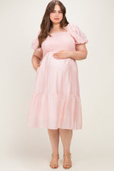 woman wearing a light pink maternity plus dress with puffed short sleeves and a tiered skirt, showing her baby bump