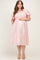 woman wearing a light pink maternity plus dress with puffed short sleeves and a tiered skirt, showing her baby bump