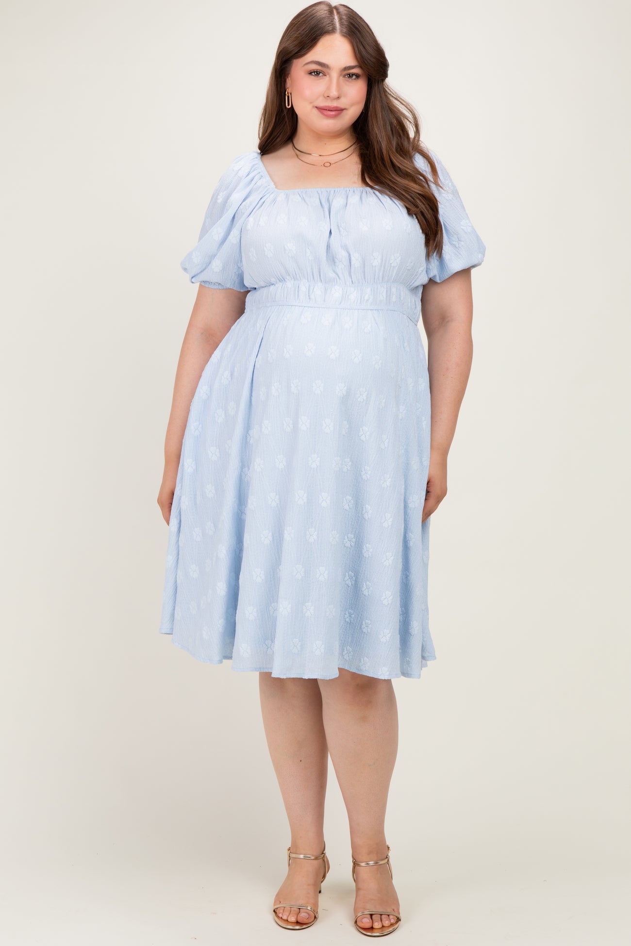 woman wearing a light blue maternity plus dress with puff sleeves and a cinched waist, showing a baby bump