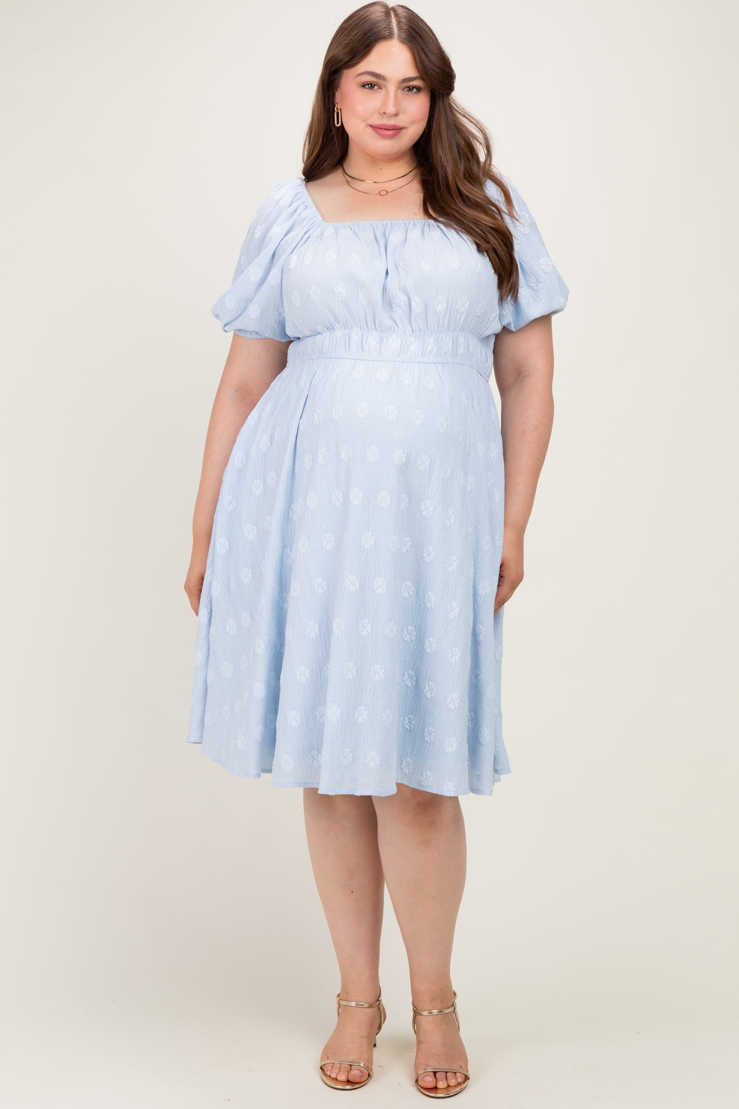 woman wearing a light blue maternity plus dress with puff sleeves and a cinched waist, showing a baby bump