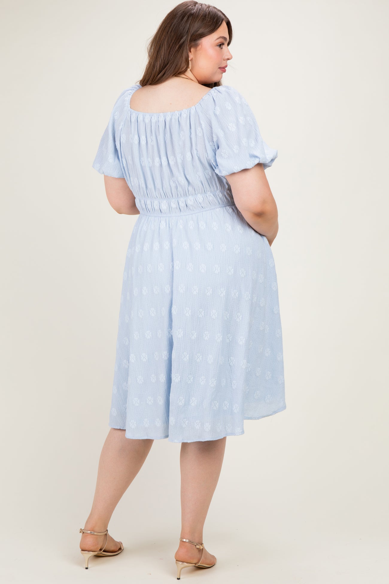 woman wearing a light blue floral print maternity dress with a fitted waist and puff sleeves, showing a baby bump