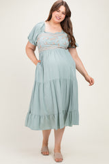 woman wearing a sage green maternity plus maxi dress with embroidered bodice and short puff sleeves, holding pockets