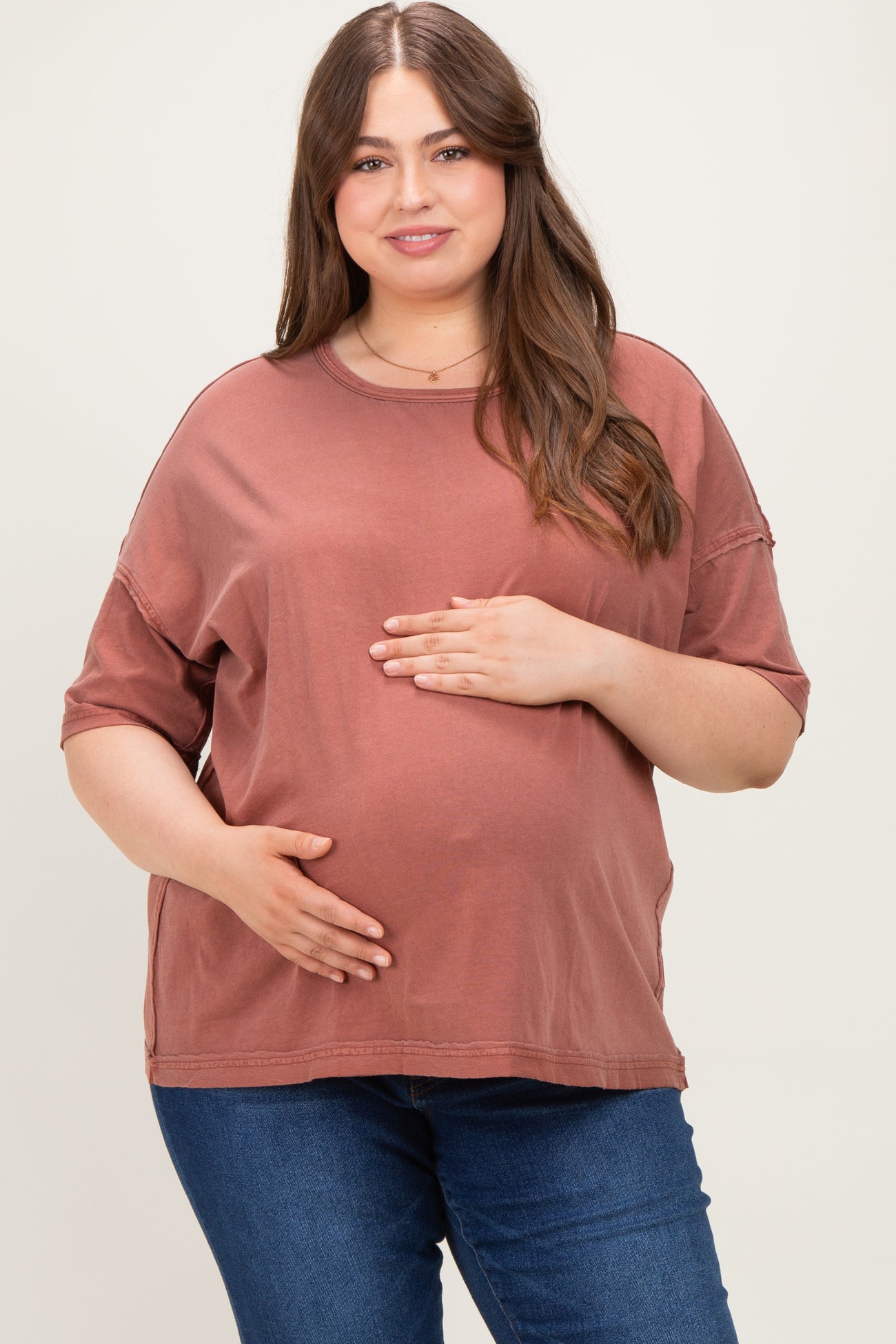 woman wearing a rust-colored maternity plus oversized t-shirt and holding her baby bump