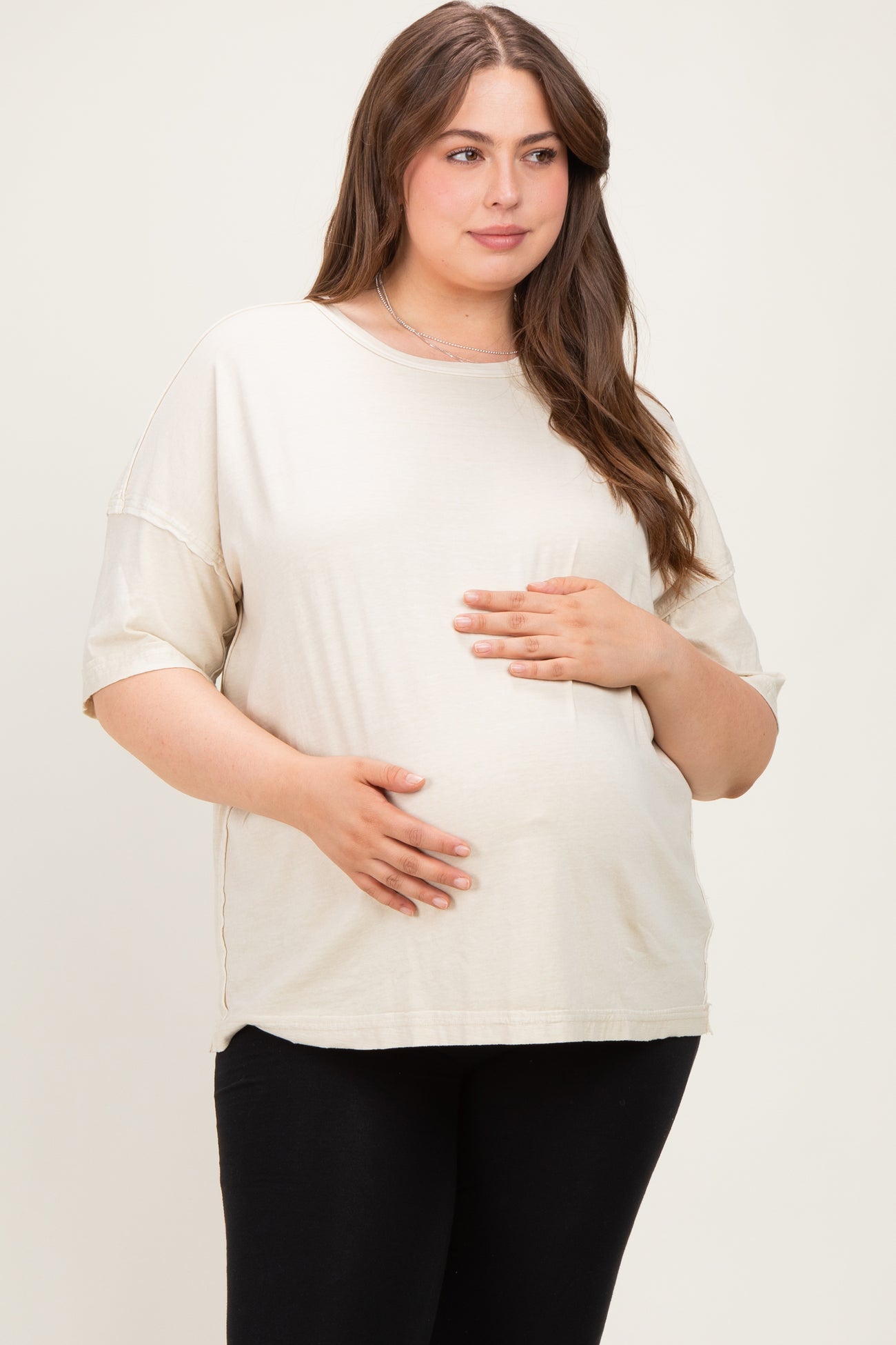 woman wearing a beige maternity plus oversized t-shirt with a visible baby bump and black leggings