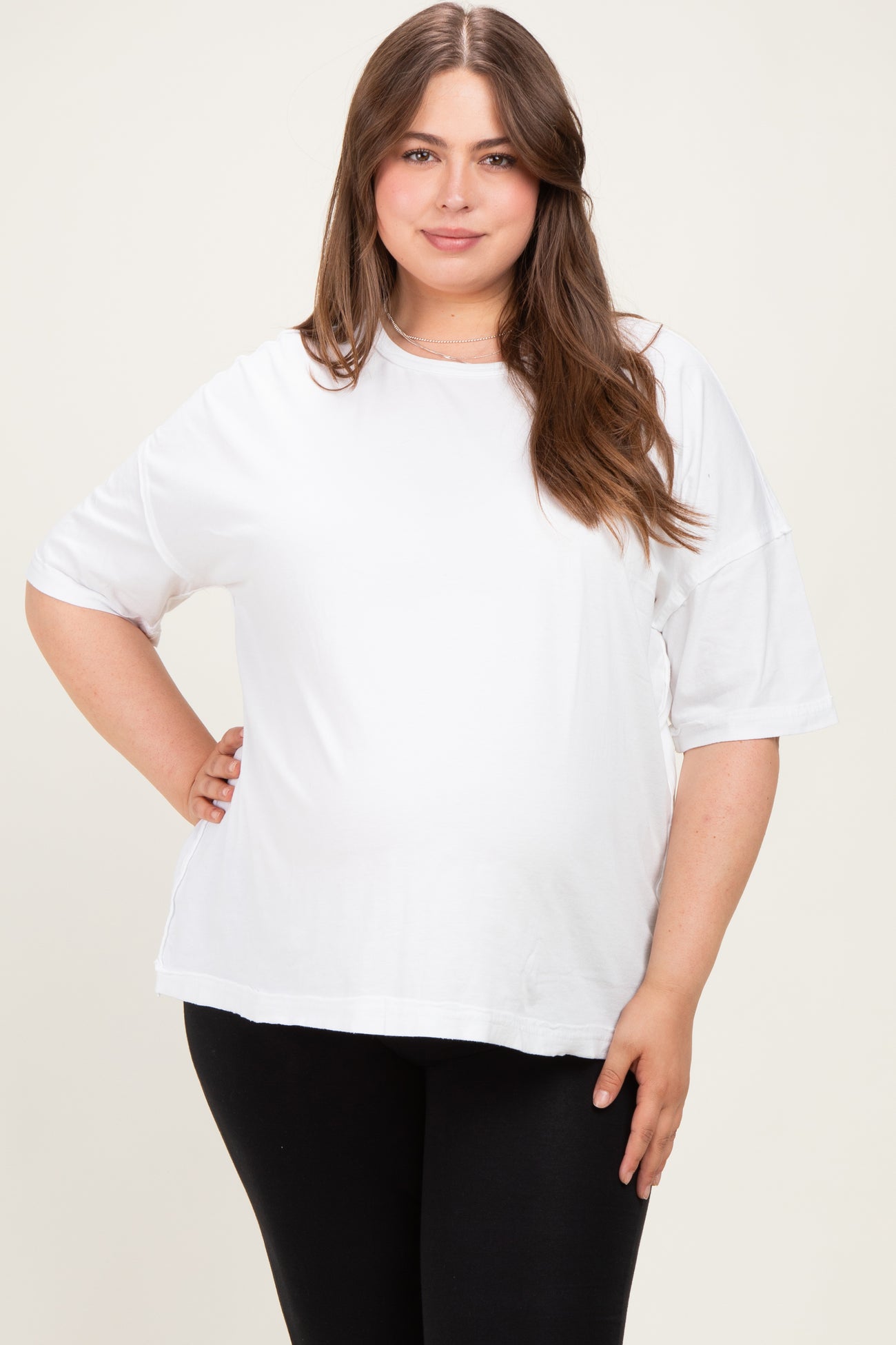 woman wearing a white maternity plus oversized t-shirt and black leggings, showing her baby bump