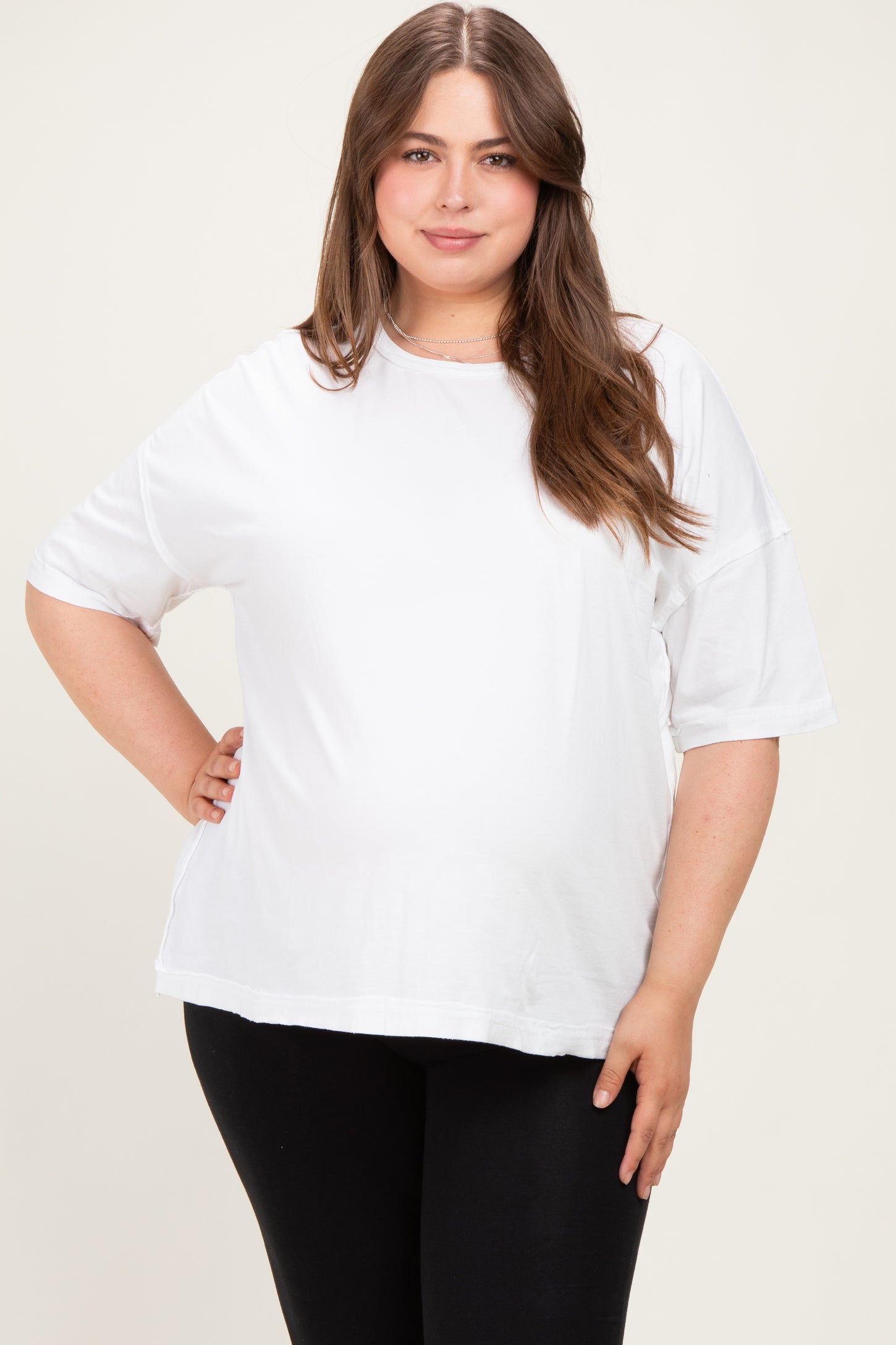 woman wearing a white maternity plus oversized t-shirt and black leggings, showing her baby bump