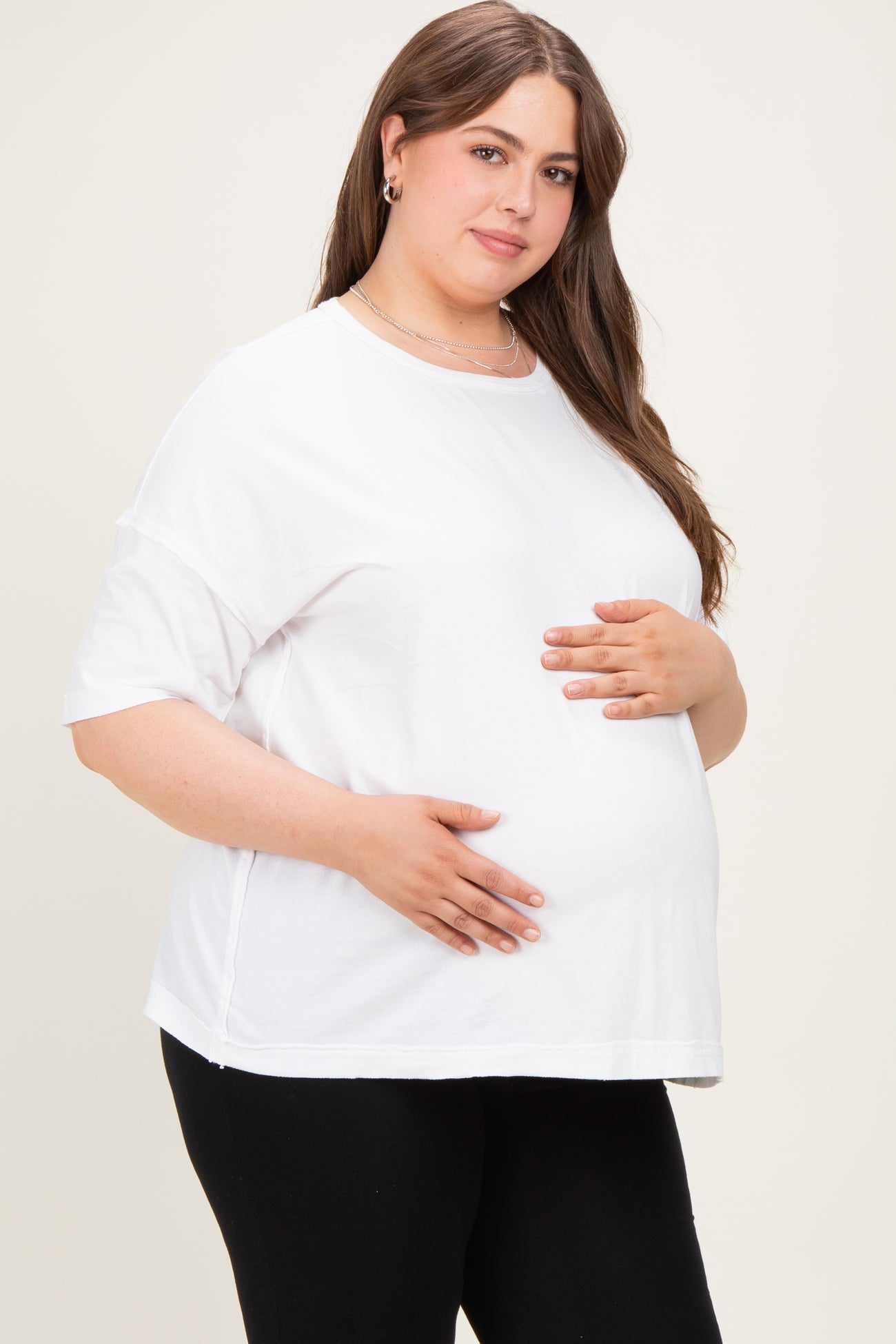 woman wearing a white short sleeve maternity top and holding her baby bump, paired with black leggings