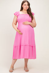woman wearing a pink maternity plus dress with smocked bodice and ruffled sleeves, holding her baby bump