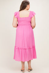 woman wearing a pink maternity plus dress with ruffle sleeves and a tiered skirt, showing her baby bump from the back