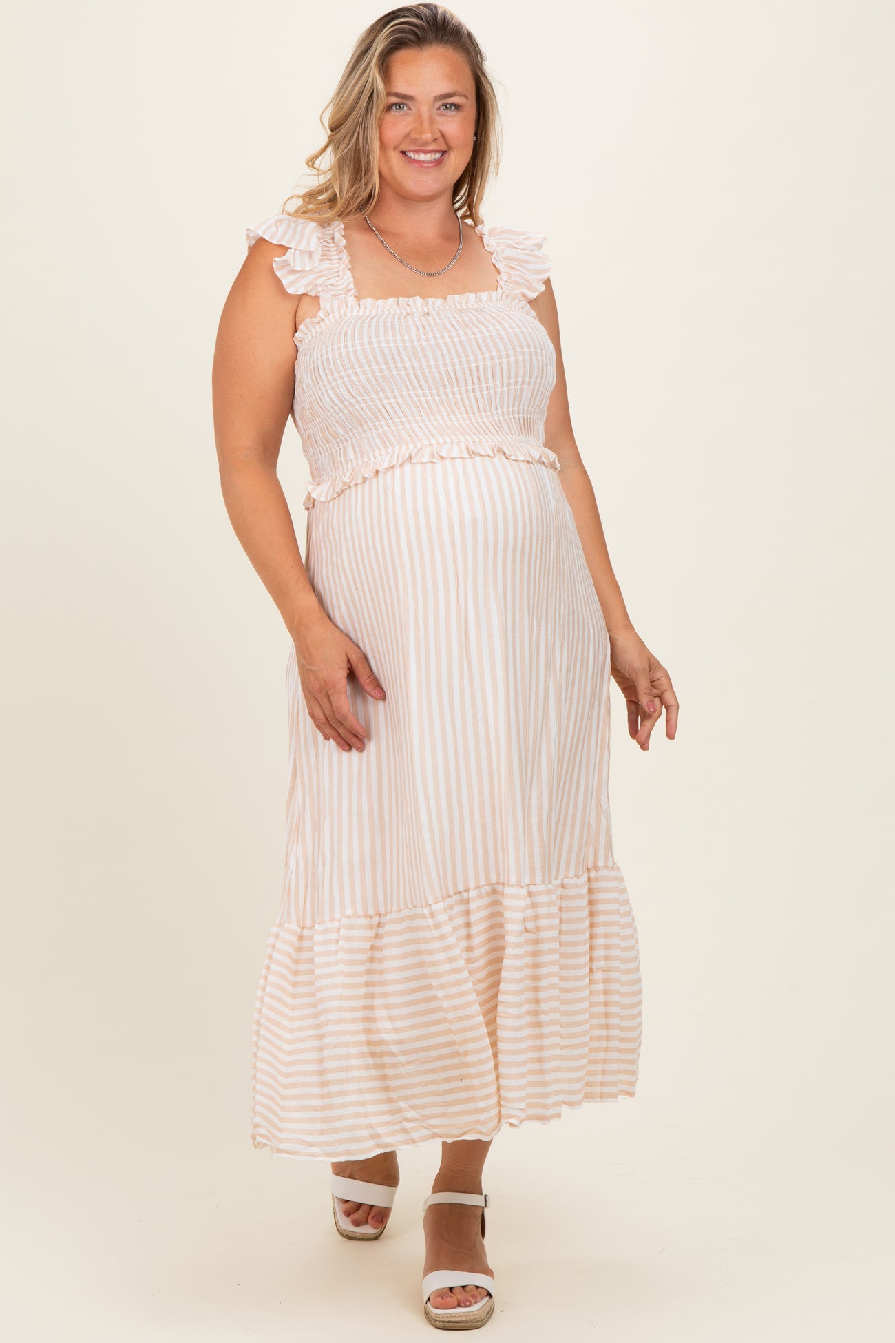 woman wearing a light pink and white striped maternity maxi dress with ruffle details and a visible baby bump
