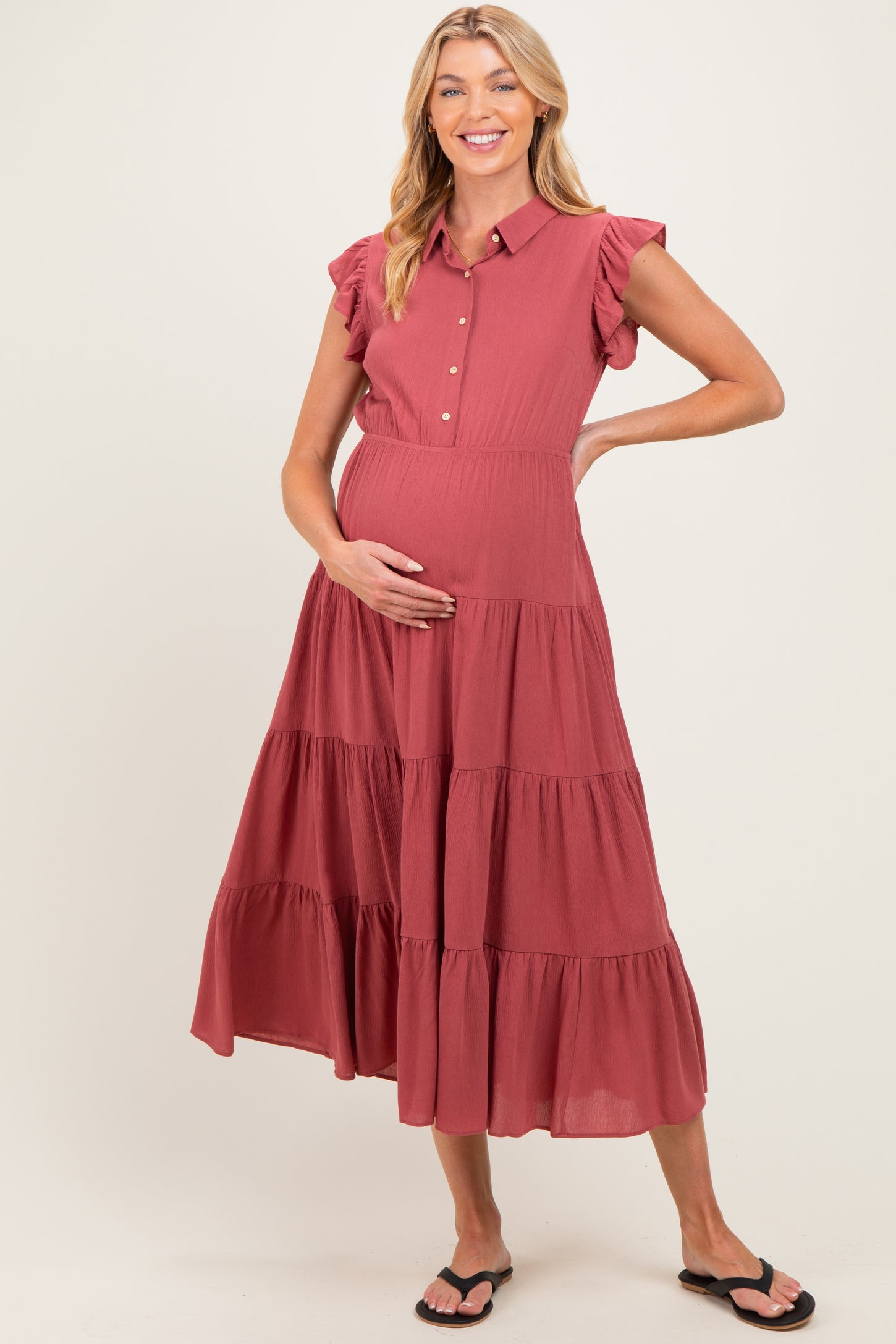 woman wearing a rust-colored maternity dress with ruffle sleeves and a tiered skirt, gently cradling her baby bump